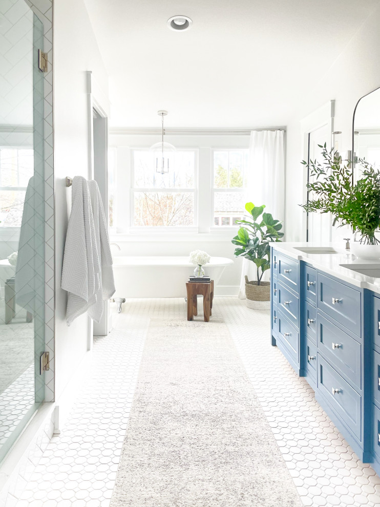 This is an example of a large transitional master bathroom in Nashville with shaker cabinets, blue cabinets, a claw-foot tub, an alcove shower, white tile, ceramic tile, grey walls, ceramic floors, an undermount sink, engineered quartz benchtops, white floor, a hinged shower door, white benchtops, a laundry, a double vanity, a built-in vanity and vaulted.