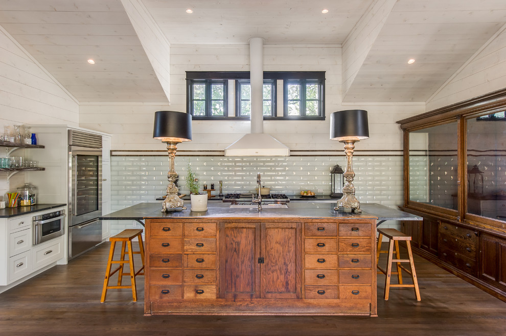 Photo of a country kitchen in Austin with shaker cabinets, white cabinets, white splashback, subway tile splashback, stainless steel appliances, dark hardwood floors and with island.