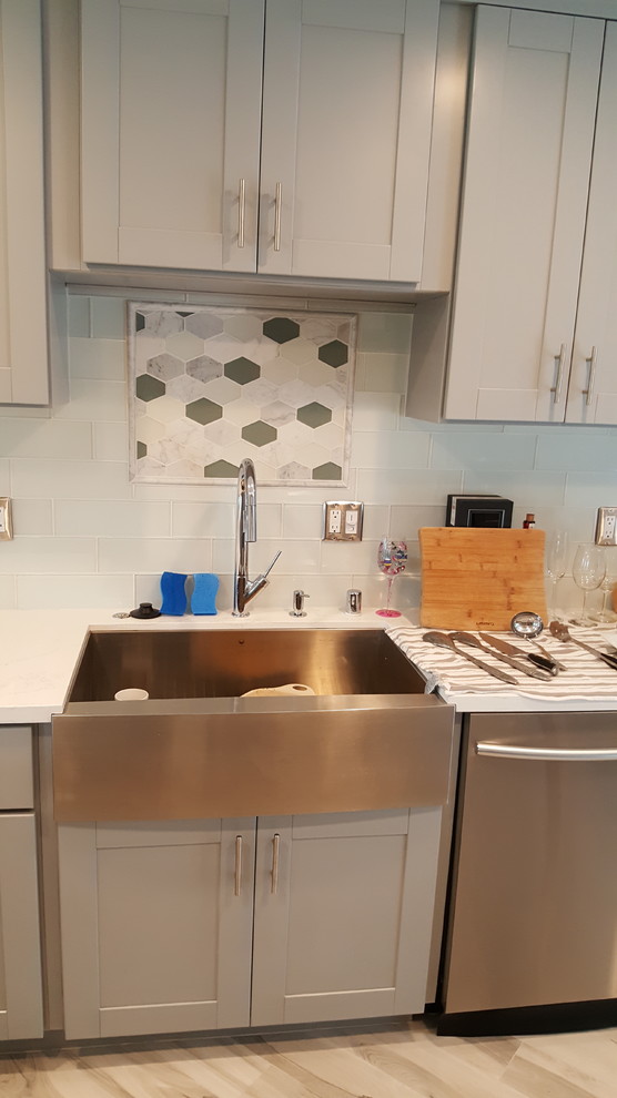 This is an example of a mid-sized transitional kitchen in San Diego with a farmhouse sink, shaker cabinets, grey cabinets, white splashback, subway tile splashback, stainless steel appliances, porcelain floors and beige floor.