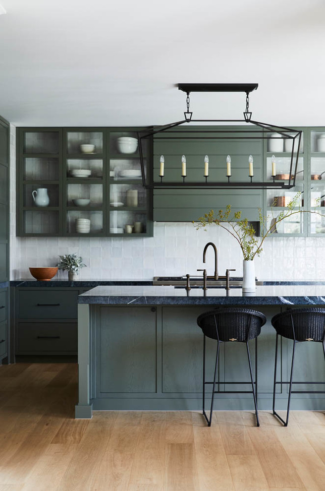 Inspiration for a transitional l-shaped kitchen in Sydney with flat-panel cabinets, green cabinets, white splashback, stainless steel appliances, light hardwood floors, with island, beige floor and black benchtop.
