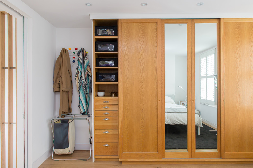 Contemporary gender-neutral built-in wardrobe in London with recessed-panel cabinets, medium wood cabinets and light hardwood floors.