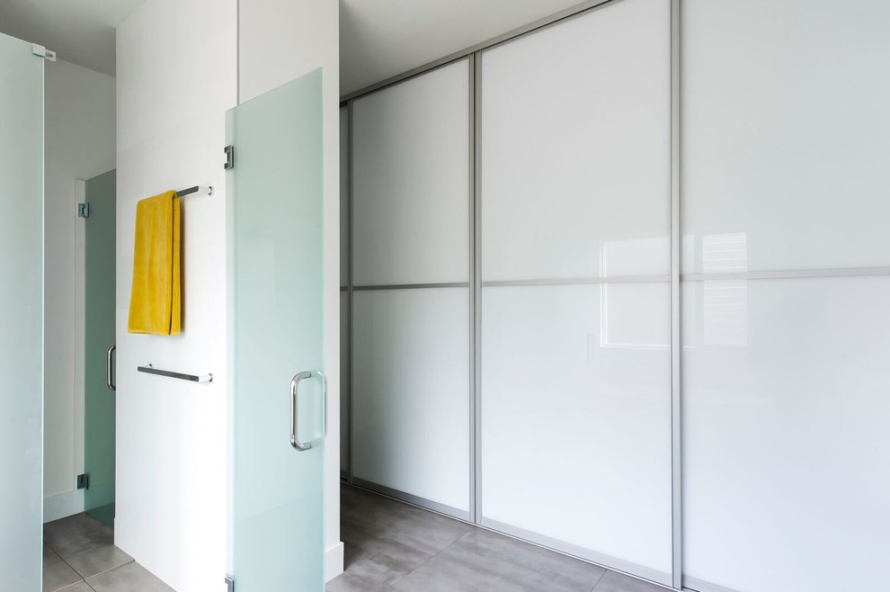 This is an example of a mid-sized contemporary gender-neutral walk-in wardrobe in Sydney with glass-front cabinets, white cabinets and concrete floors.