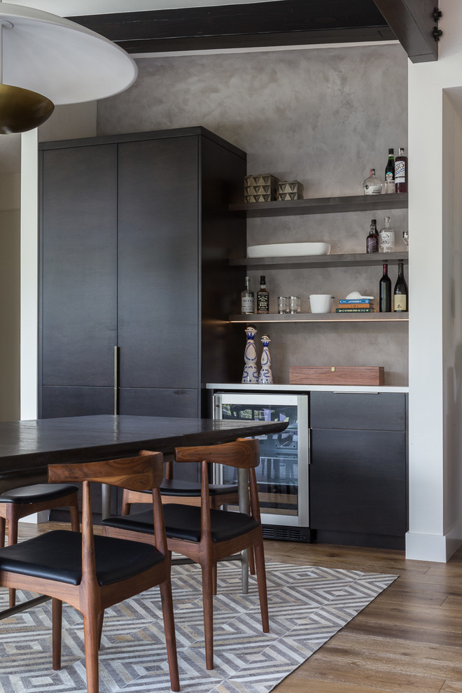 This is an example of a small country single-wall home bar in Sacramento with no sink, flat-panel cabinets, dark wood cabinets, grey splashback, light hardwood floors and white benchtop.