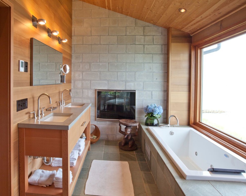 Photo of a large beach style master bathroom in Boston with a drop-in sink, flat-panel cabinets, light wood cabinets, a corner tub, gray tile, cement tile, grey walls, slate floors and concrete benchtops.