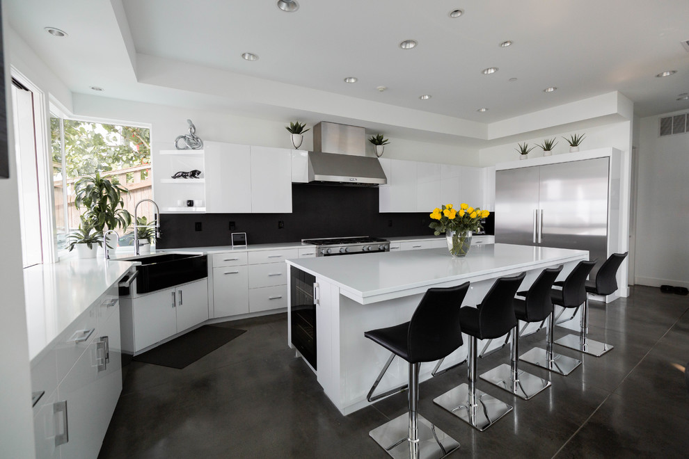 Inspiration for a contemporary l-shaped kitchen in Seattle with a farmhouse sink, flat-panel cabinets, black splashback, stainless steel appliances, concrete floors, with island, grey floor and white benchtop.