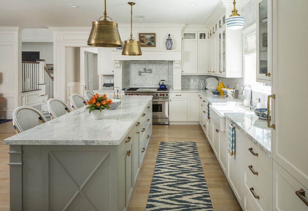 This is an example of a traditional l-shaped kitchen in Salt Lake City with a farmhouse sink, shaker cabinets, white cabinets, white splashback, panelled appliances, light hardwood floors, with island, brown floor and white benchtop.