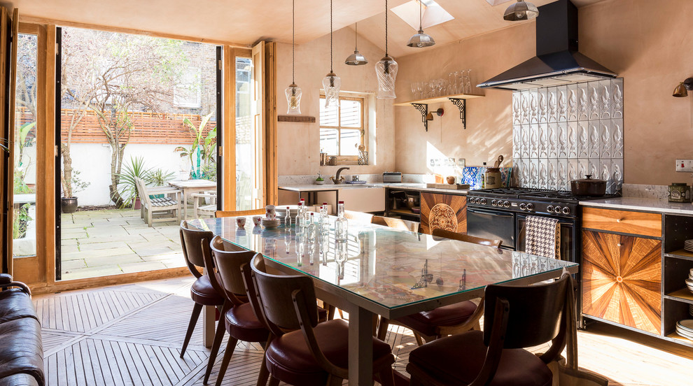 Large bohemian single-wall kitchen/diner in London with a submerged sink, flat-panel cabinets, medium wood cabinets, marble worktops, metallic splashback, metal splashback, black appliances, medium hardwood flooring and no island.