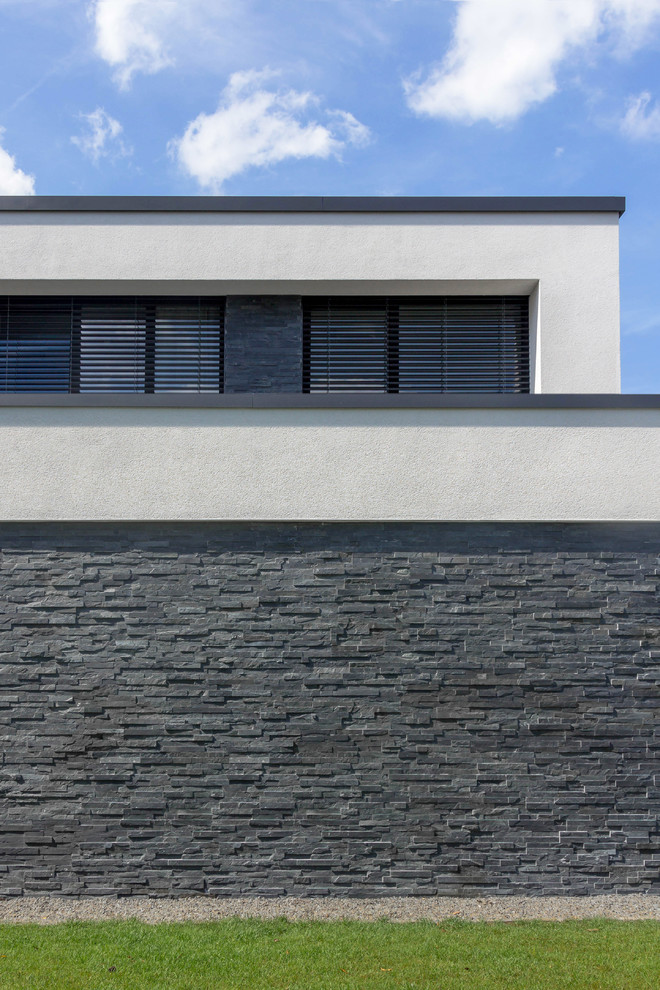 Design ideas for a mid-sized contemporary two-storey black house exterior in Cologne with stone veneer and a flat roof.
