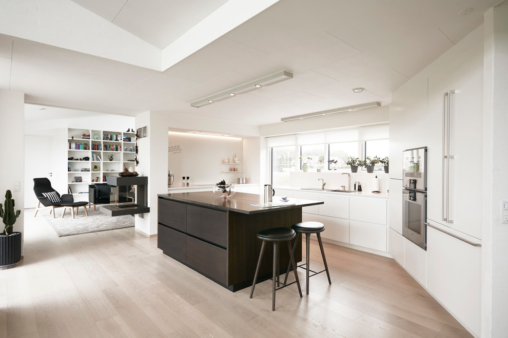This is an example of a large modern galley open plan kitchen in Esbjerg with a drop-in sink, flat-panel cabinets, quartzite benchtops, stainless steel appliances, light hardwood floors and with island.