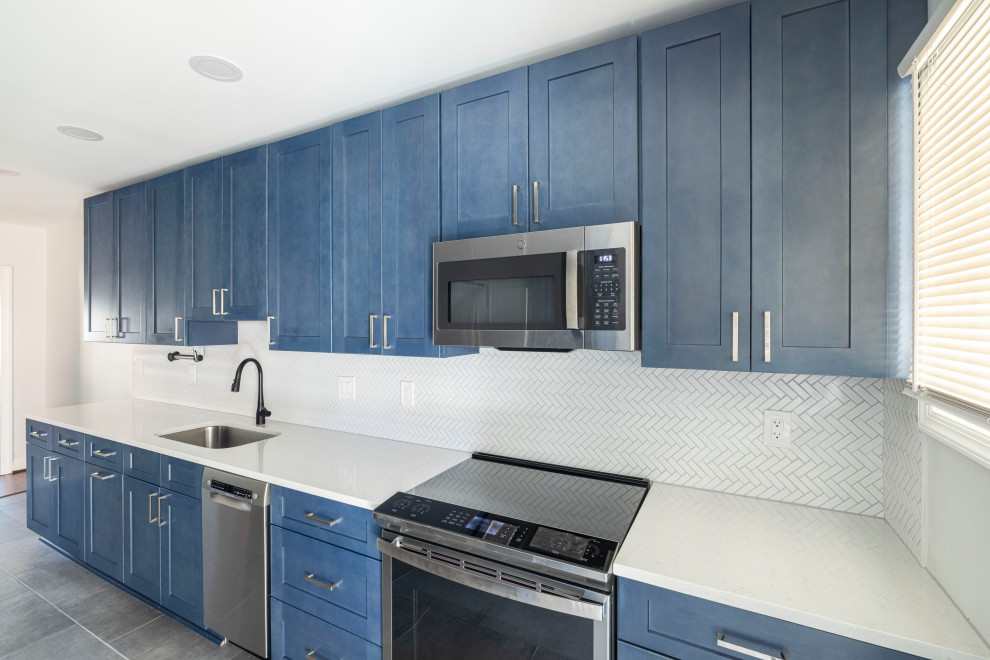 Inredning av ett modernt mellanstort vit vitt kök, med en undermonterad diskho, skåp i shakerstil, blå skåp, bänkskiva i kvarts, vitt stänkskydd, stänkskydd i mosaik, rostfria vitvaror, klinkergolv i porslin och grått golv