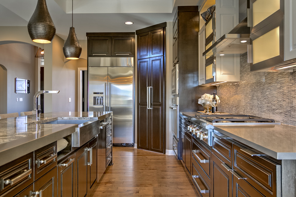 Large contemporary l-shaped open plan kitchen in Omaha with a farmhouse sink, raised-panel cabinets, dark wood cabinets, grey splashback, stainless steel appliances, light hardwood floors, with island and beige floor.