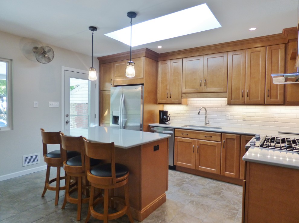 Inspiration for a transitional l-shaped porcelain tile eat-in kitchen remodel with an undermount sink, recessed-panel cabinets, medium tone wood cabinets, quartz countertops, white backsplash, subway tile backsplash, stainless steel appliances and an island