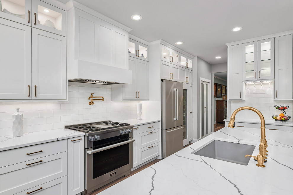 Inspiration for a contemporary medium tone wood floor and brown floor eat-in kitchen remodel with a single-bowl sink, shaker cabinets, white cabinets, quartz countertops, white backsplash, subway tile backsplash, stainless steel appliances, an island and white countertops