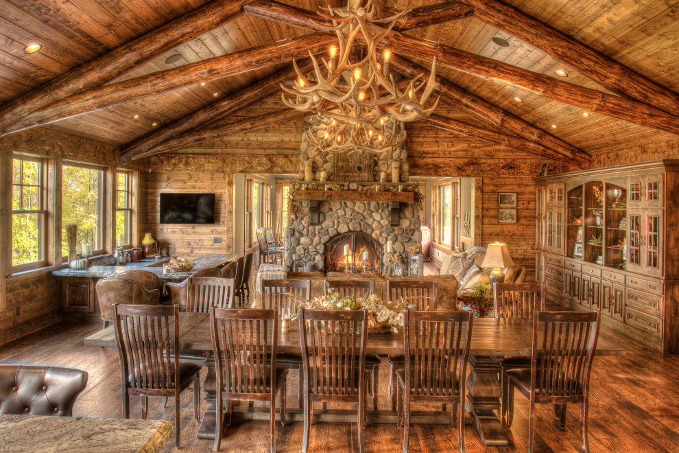 Inspiration pour une grande salle à manger ouverte sur le salon chalet en bois avec un mur marron, un sol en bois brun, une cheminée standard, un manteau de cheminée en pierre, un sol marron et un plafond voûté.