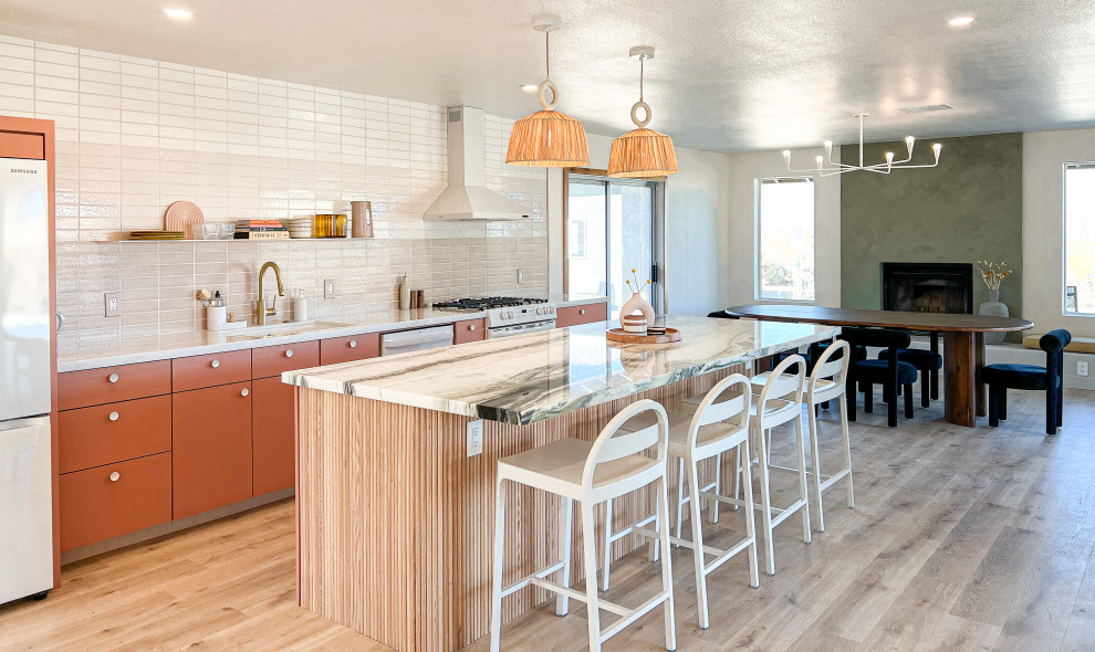 Contemporary single-wall eat-in kitchen in Los Angeles with an undermount sink, flat-panel cabinets, pink cabinets, marble benchtops, pink splashback, ceramic splashback, white appliances, light hardwood floors, with island, brown floor and multi-coloured benchtop.