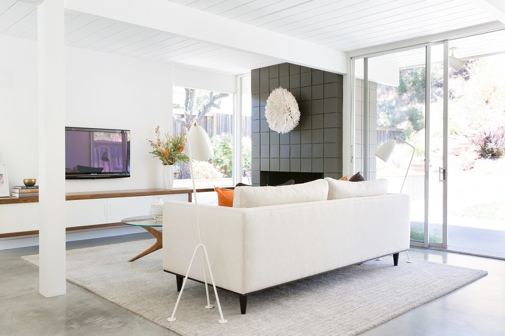 Eclectic open concept living room in San Francisco with white walls, concrete floors, a standard fireplace, a concrete fireplace surround and a wall-mounted tv.
