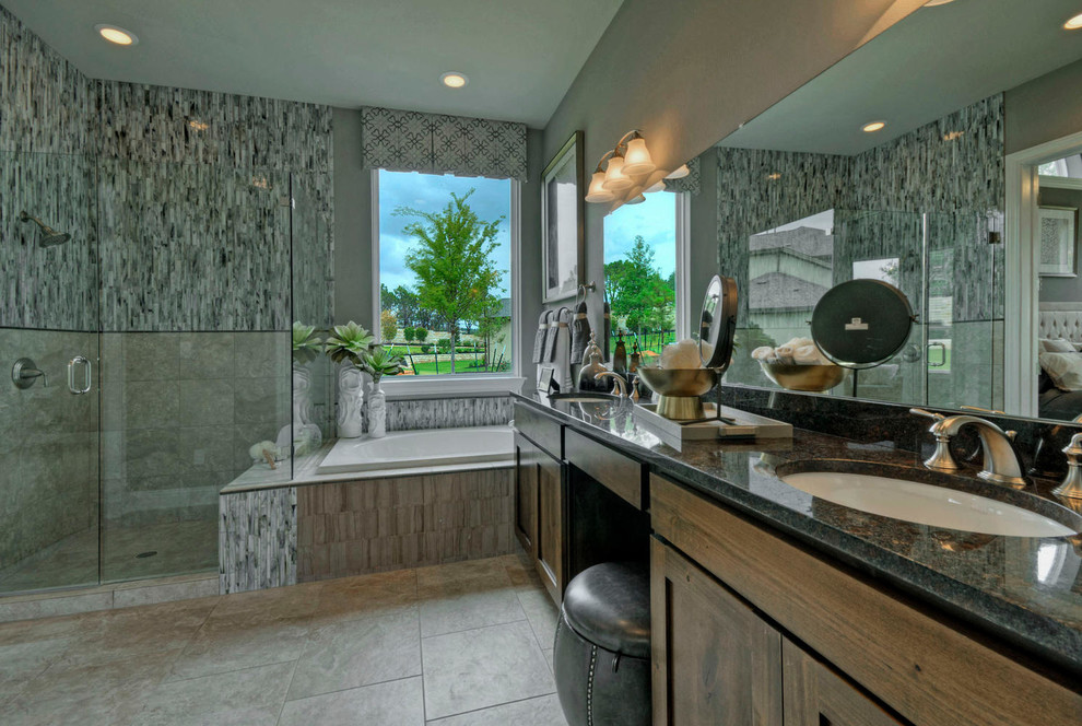 This is an example of a mid-sized transitional master bathroom in Austin with a drop-in sink, flat-panel cabinets, medium wood cabinets, granite benchtops, a drop-in tub, an open shower, a one-piece toilet, gray tile, glass tile, grey walls and porcelain floors.