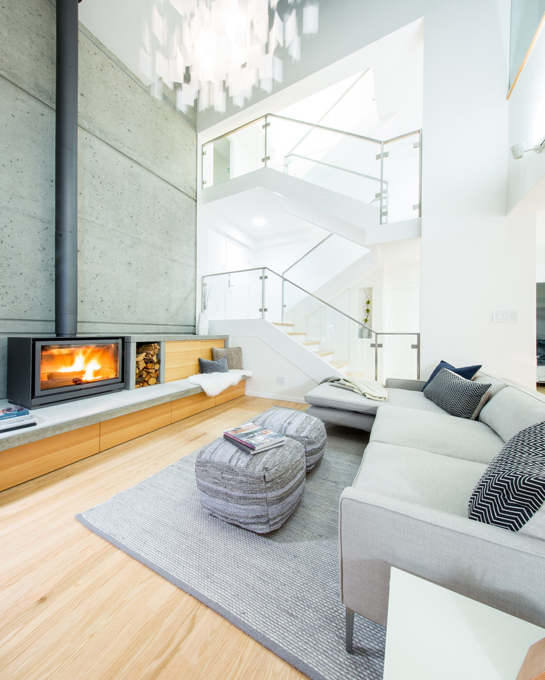 This is an example of a contemporary open concept family room in Vancouver with white walls, light hardwood floors, a wood stove and a metal fireplace surround.