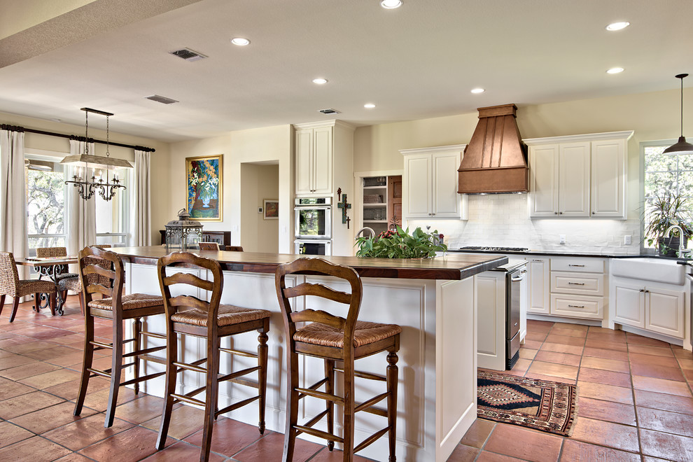 Large galley eat-in kitchen in Austin with white cabinets, white splashback, stainless steel appliances, terra-cotta floors, multiple islands and granite benchtops.