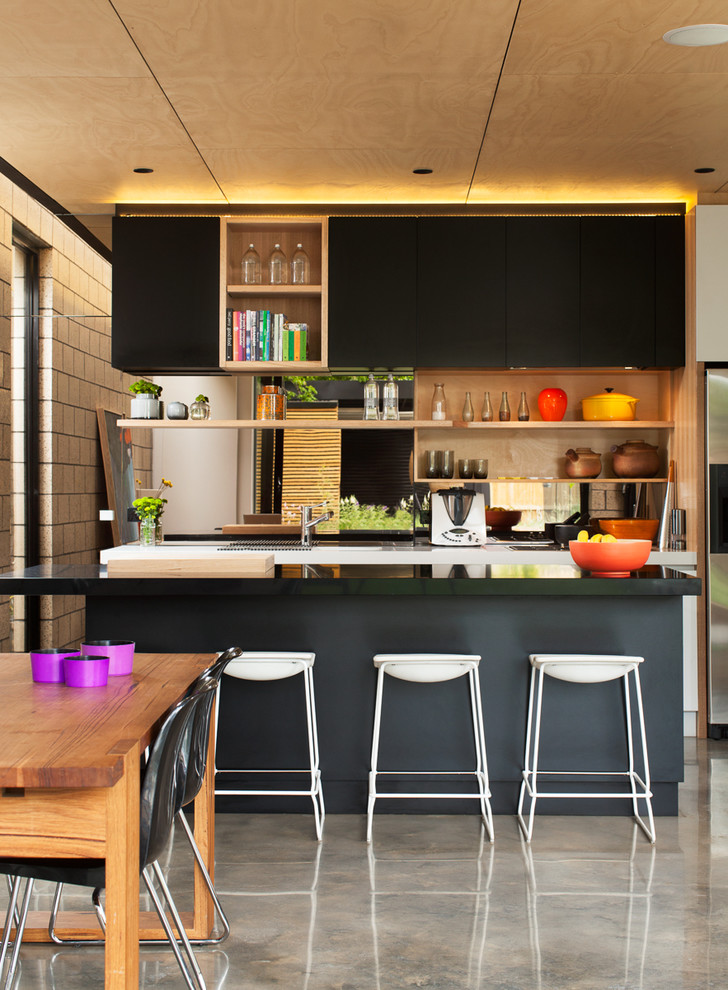 Mid-sized contemporary galley eat-in kitchen in Melbourne with black cabinets, granite benchtops, concrete floors, with island and flat-panel cabinets.