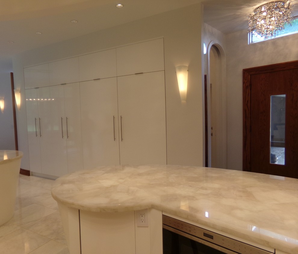 Expansive contemporary u-shaped kitchen pantry in New York with a farmhouse sink, flat-panel cabinets, white cabinets, quartz benchtops, white splashback, stone slab splashback, panelled appliances, porcelain floors and with island.