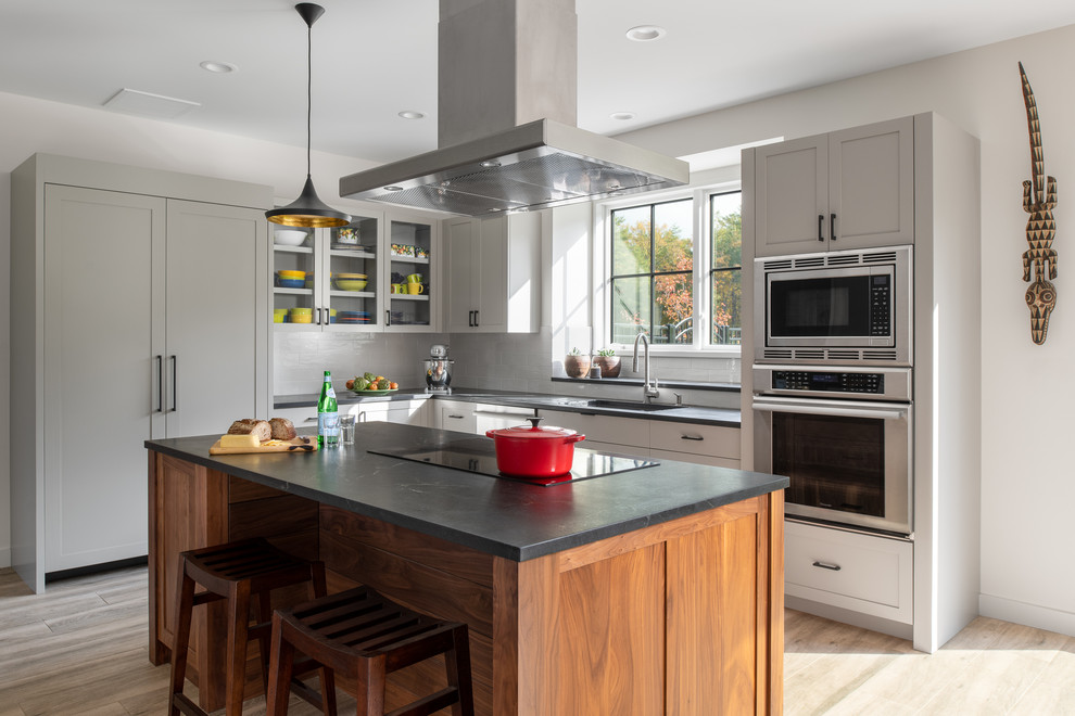 Mid-sized country l-shaped eat-in kitchen in Burlington with an undermount sink, shaker cabinets, grey cabinets, soapstone benchtops, white splashback, subway tile splashback, stainless steel appliances, porcelain floors, with island, beige floor and black benchtop.