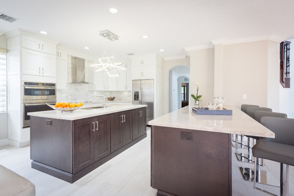 Large transitional l-shaped porcelain tile open concept kitchen photo in Miami with an undermount sink, shaker cabinets, white cabinets, subway tile backsplash, stainless steel appliances and two islands