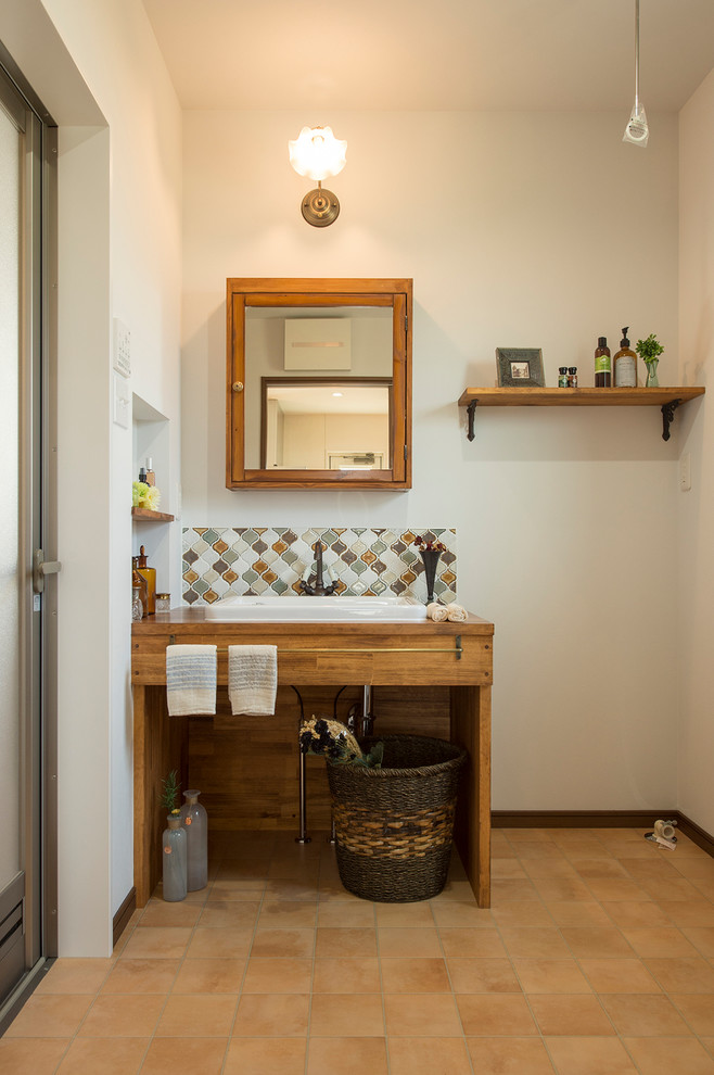 This is an example of a mediterranean powder room in Other with glass-front cabinets, white walls, terra-cotta floors and brown floor.