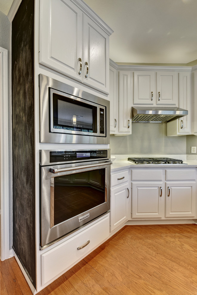 Example of a mid-sized transitional u-shaped light wood floor eat-in kitchen design in Austin with an undermount sink, white cabinets, quartz countertops, white backsplash, stone slab backsplash, stainless steel appliances, a peninsula and raised-panel cabinets