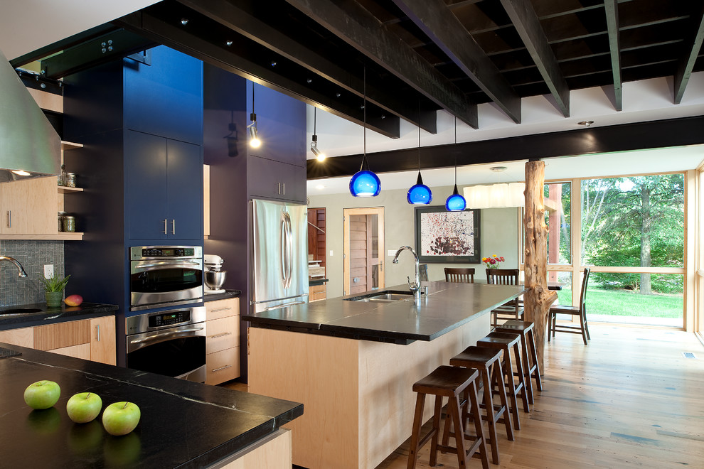 This is an example of a large contemporary l-shaped eat-in kitchen in DC Metro with a double-bowl sink, flat-panel cabinets, light wood cabinets, granite benchtops, stainless steel appliances, light hardwood floors, with island, glass tile splashback and black benchtop.