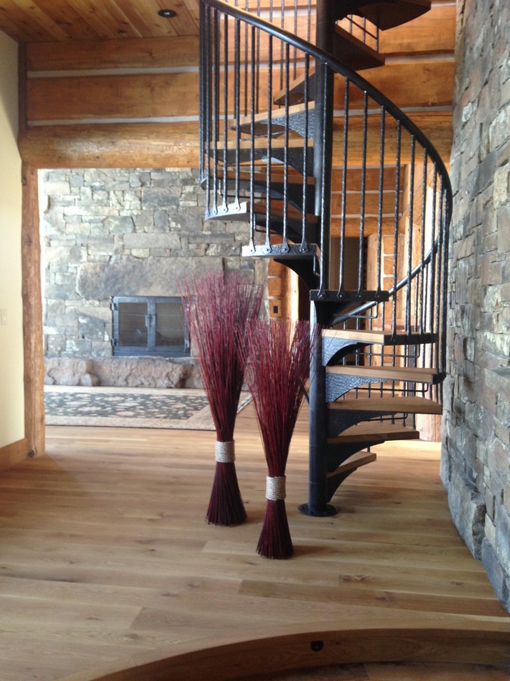 Example of a large mountain style open concept light wood floor staircase design with a standard fireplace and a stone fireplace