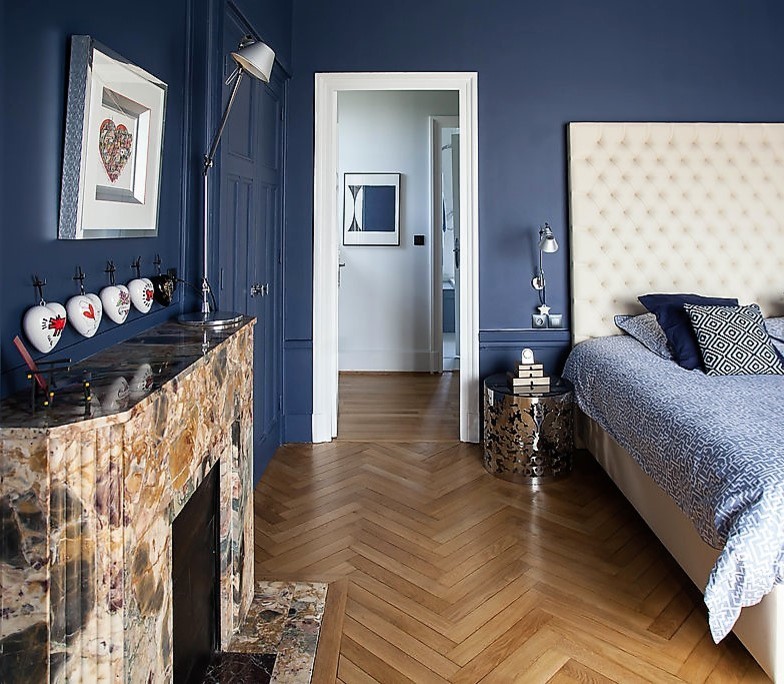 Design ideas for a mid-sized transitional master bedroom in Lyon with blue walls, light hardwood floors, a standard fireplace, a stone fireplace surround and beige floor.