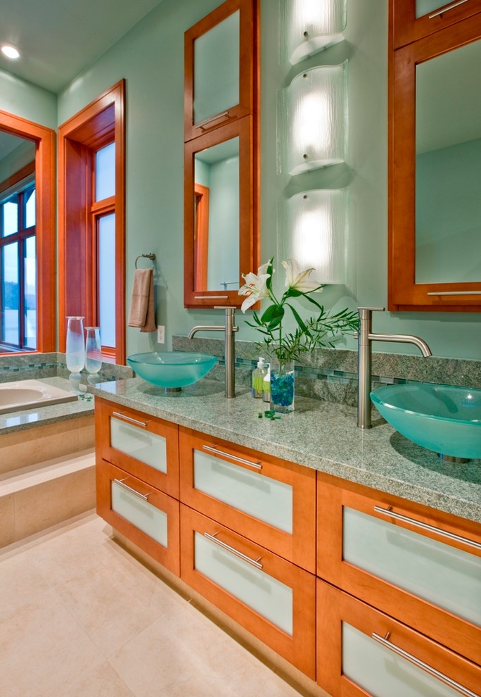 This is an example of a contemporary master bathroom in Seattle with a vessel sink, glass-front cabinets, medium wood cabinets, a drop-in tub, green tile, granite benchtops, green walls and green benchtops.