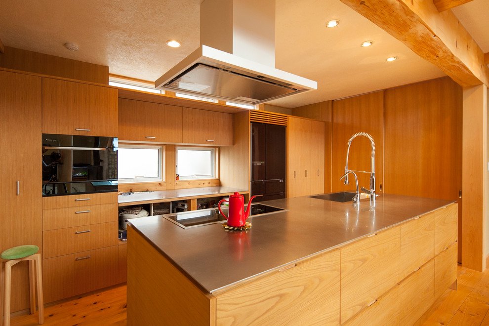 This is an example of an asian single-wall open plan kitchen in Other with a single-bowl sink, flat-panel cabinets, medium wood cabinets, stainless steel benchtops, medium hardwood floors, with island and brown floor.