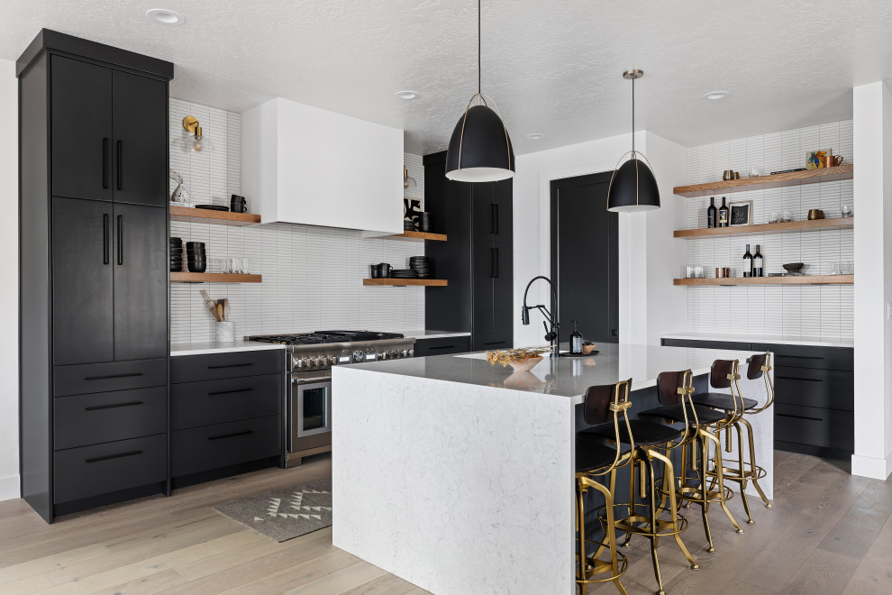 This is an example of a mid-sized scandinavian l-shaped open plan kitchen in Boise with an undermount sink, flat-panel cabinets, black cabinets, quartzite benchtops, white splashback, subway tile splashback, stainless steel appliances, light hardwood floors, with island, beige floor, white benchtop and exposed beam.