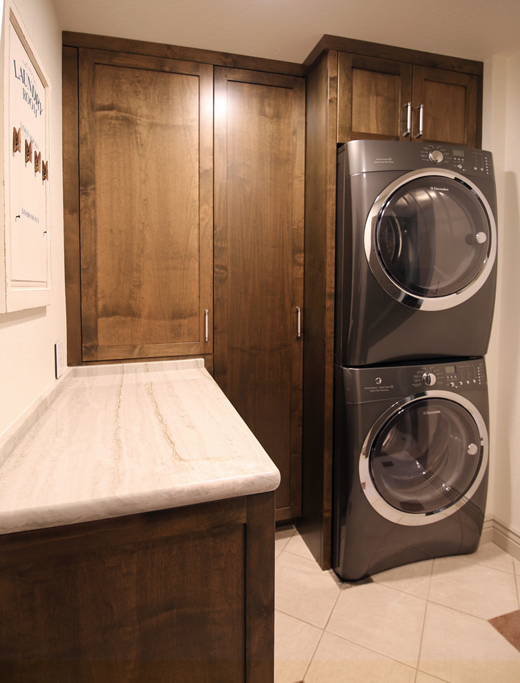 Design ideas for a mid-sized transitional l-shaped dedicated laundry room in San Francisco with shaker cabinets, dark wood cabinets, quartzite benchtops, white walls, porcelain floors and a stacked washer and dryer.