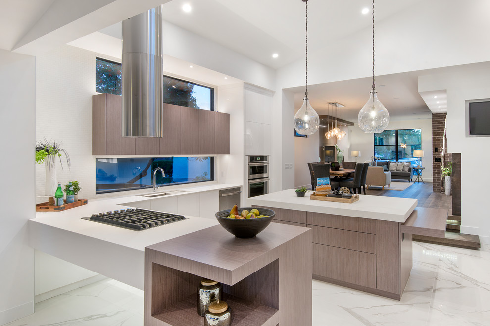 Example of a large minimalist marble floor and white floor kitchen design in Calgary with flat-panel cabinets, white backsplash, stainless steel appliances, an island and white countertops