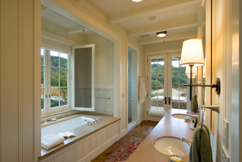 Design ideas for a large country master bathroom in San Francisco with louvered cabinets, white cabinets, an undermount tub, an alcove shower, a two-piece toilet, white tile, subway tile, white walls, medium hardwood floors, an undermount sink and solid surface benchtops.