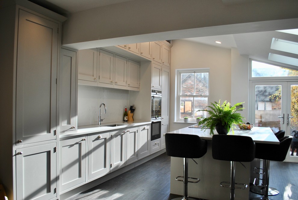 This is an example of a mid-sized traditional open plan kitchen in Hertfordshire with shaker cabinets, grey cabinets, with island and black floor.