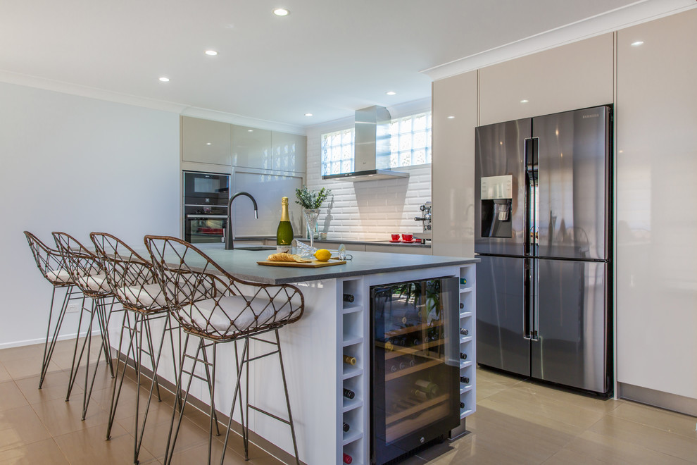 This is an example of a large contemporary l-shaped open plan kitchen in Brisbane with an undermount sink, beige cabinets, quartz benchtops, white splashback, subway tile splashback, stainless steel appliances, porcelain floors, with island and brown floor.