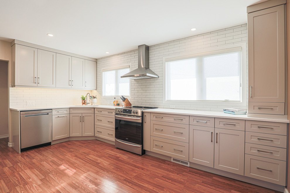 Example of a mid-sized transitional l-shaped vinyl floor and brown floor eat-in kitchen design in Edmonton with an undermount sink, shaker cabinets, beige cabinets, quartz countertops, white backsplash, ceramic backsplash, stainless steel appliances, no island and white countertops