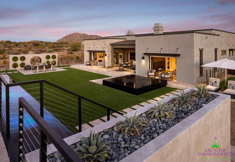 Large and desert look modern backyard partial sun xeriscape in Phoenix with natural stone pavers and a metal fence for summer.