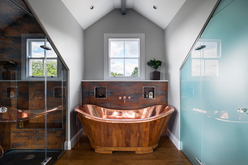 Design ideas for a large industrial master bathroom in London with medium hardwood floors, flat-panel cabinets, beige cabinets, a freestanding tub, a curbless shower, grey walls, tile benchtops, brown floor, a hinged shower door and white benchtops.