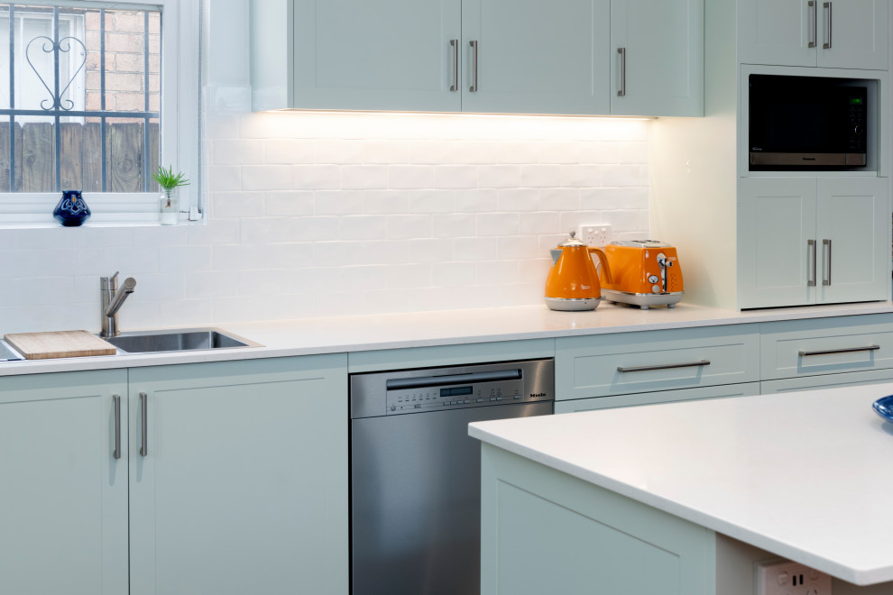 Mid-sized modern l-shaped kitchen pantry in Sydney with blue cabinets, quartz benchtops, white splashback, ceramic splashback, stainless steel appliances, with island and white benchtop.