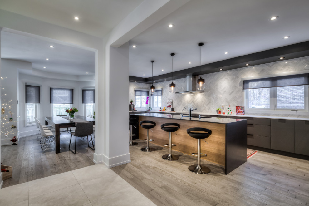 Design ideas for a large modern galley eat-in kitchen in Toronto with an undermount sink, flat-panel cabinets, grey cabinets, white splashback, marble splashback, stainless steel appliances, medium hardwood floors, with island, grey floor and black benchtop.