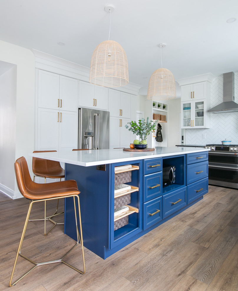 Kitchen pantry - large transitional l-shaped brown floor kitchen pantry idea in Baltimore with a drop-in sink, shaker cabinets, white cabinets, quartz countertops, white backsplash, ceramic backsplash, stainless steel appliances, an island and white countertops