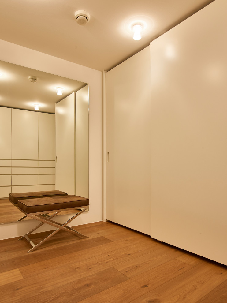 Foto di un'ampia cabina armadio unisex contemporanea con ante con riquadro incassato, ante bianche, parquet chiaro, pavimento marrone e soffitto ribassato