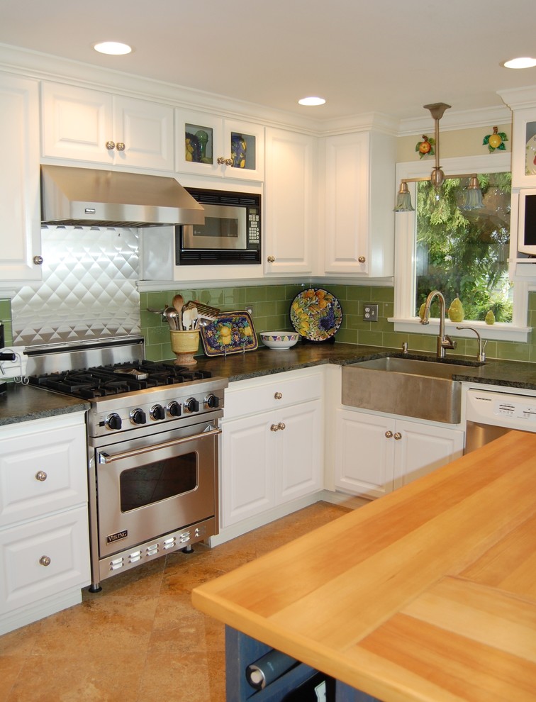 Photo of a traditional kitchen in Denver with stainless steel appliances, a farmhouse sink, wood benchtops, green splashback, glass tile splashback and white cabinets.