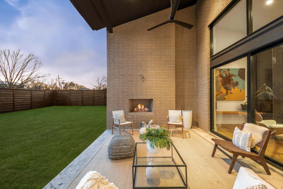 Photo of a large midcentury backyard verandah in Dallas with with fireplace, concrete slab and a roof extension.