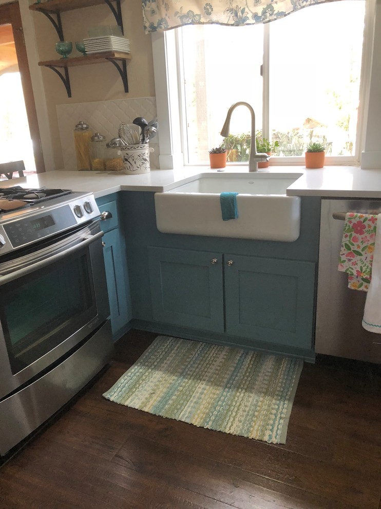 Design ideas for a mid-sized beach style l-shaped kitchen pantry in Seattle with a farmhouse sink, shaker cabinets, turquoise cabinets, quartzite benchtops, white splashback, mosaic tile splashback, stainless steel appliances, laminate floors, a peninsula, brown floor and white benchtop.